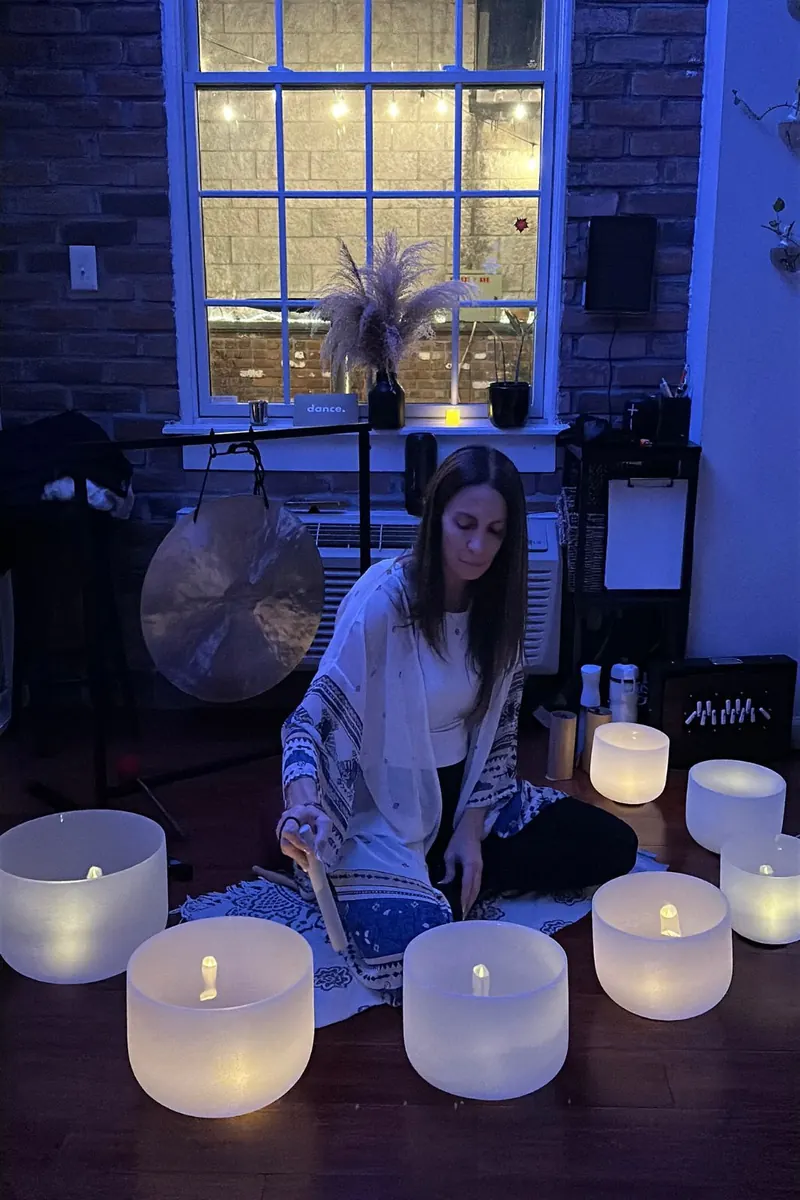 Sound practitioner playing crystal singing bowls by candlelight