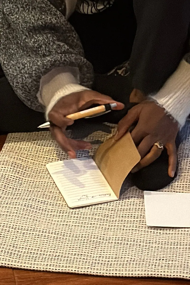 Hands writing in a journal on a woven mat during a women's circle